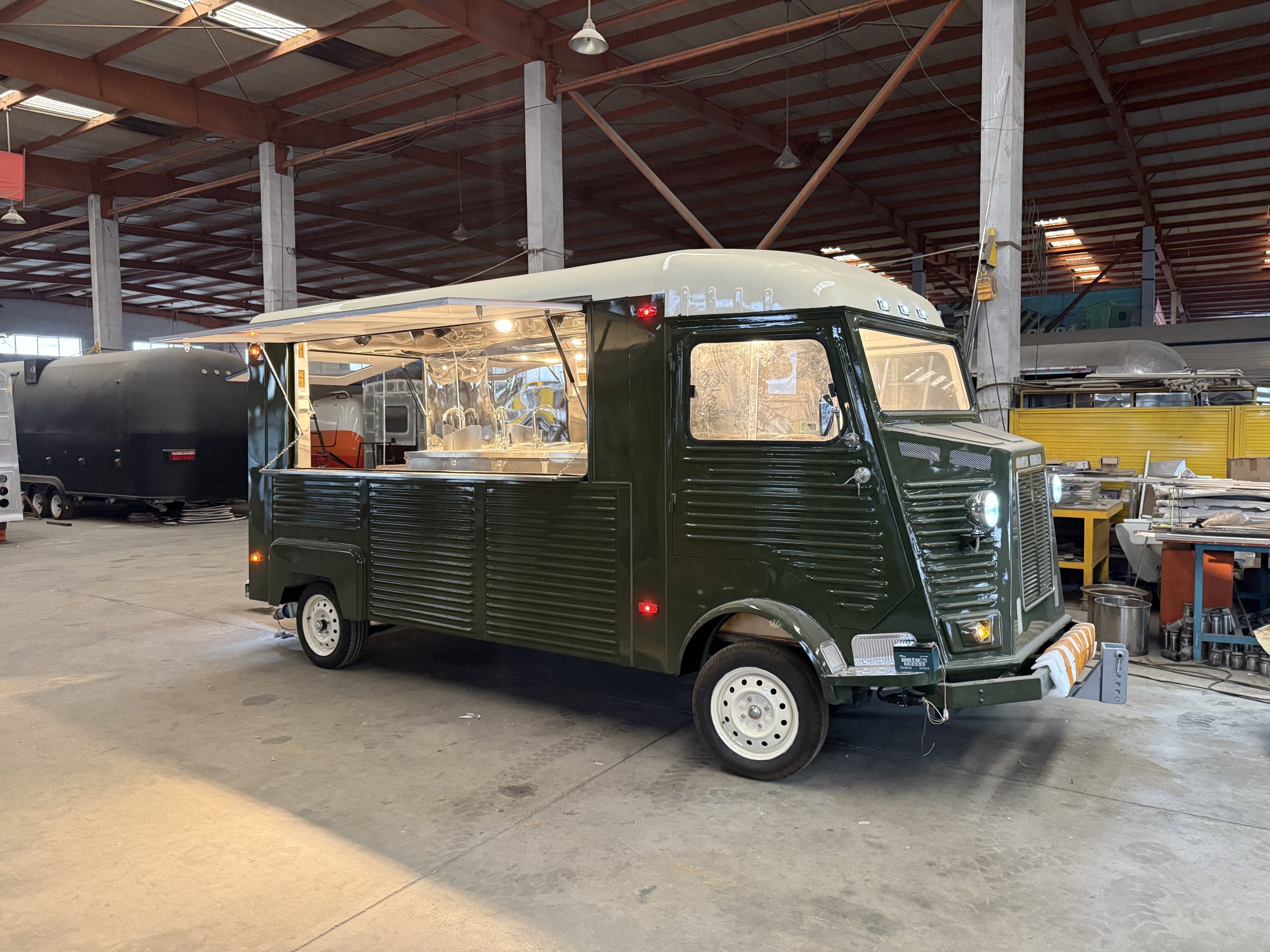 Dark green retro Citroën-style food trailer shown from a front-side angle with large serving window and stainless steel interior