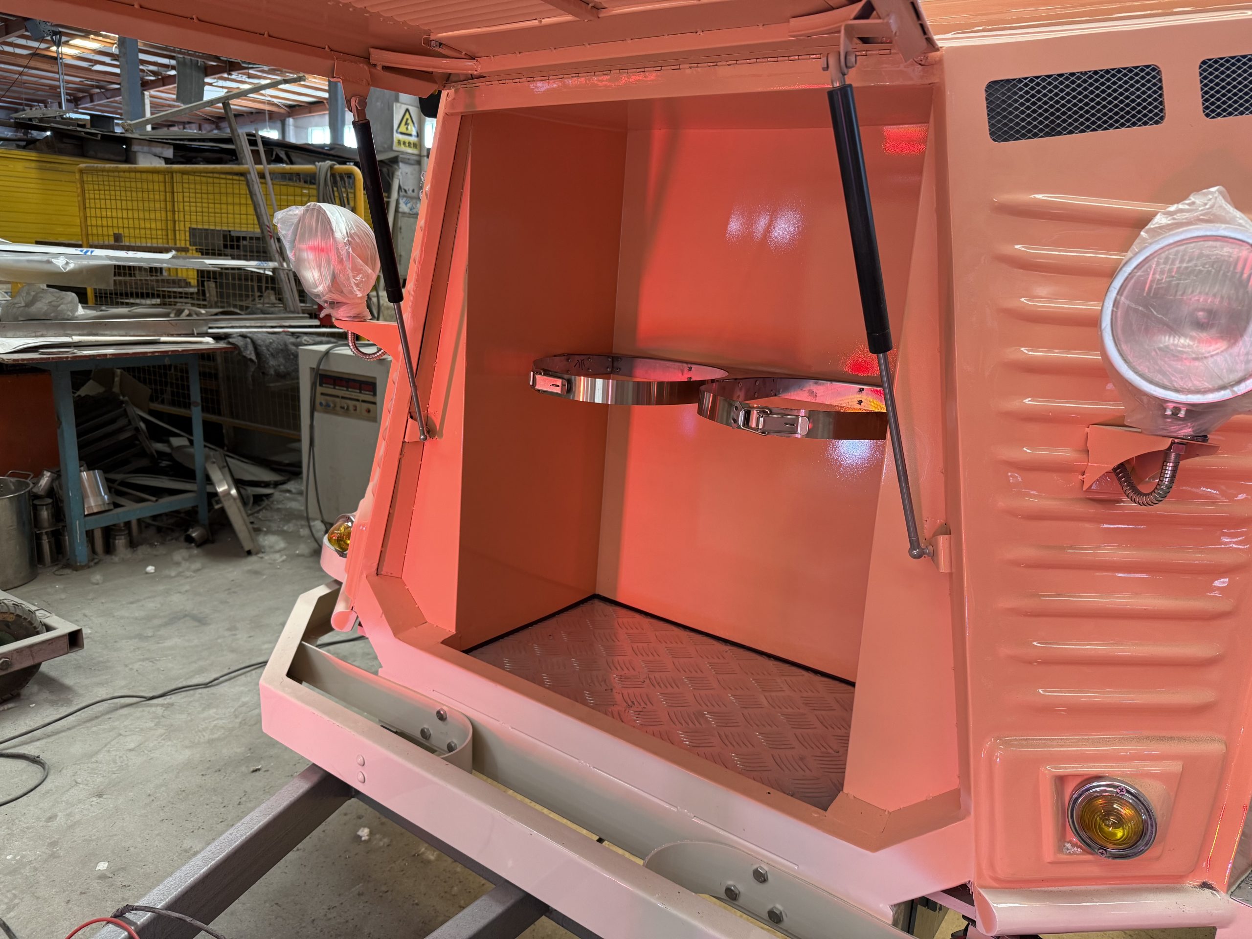 Front nose cone compartment of Citroën H food trailer opened by gas struts, featuring two stainless steel rotating trays for LPG tank storage and diamond plate flooring.